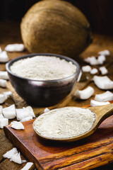 full rustic wooden spoon and coconut flour, on wooden table with coconut in the background, culinary ingredient.