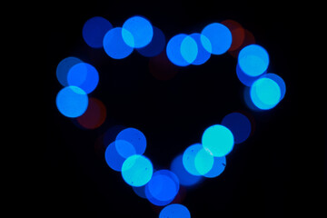 Festive background of multicolored bokeh in the shape of a heart. Abstract blurred colored lights.