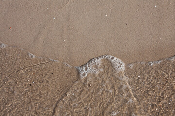 Fototapeta na wymiar Close-up of a sea wave on a sandy beach. Top view. Sand beach texture.