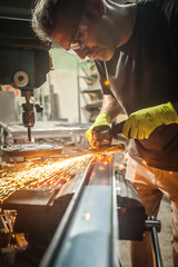 Man working with electric grinder tool on steel structure in factory, sparks flying. Grinding machine in action