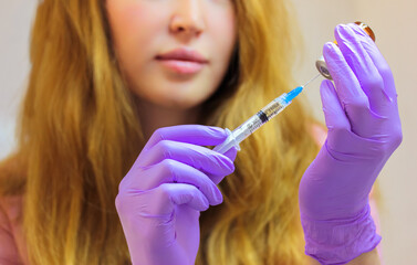 A young woman doctor wearing purple rubber gloves holds an injection syringe with a thin needle....