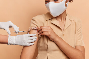 Cropped shot of dark skinned female model wears protective disposable face mask and dress gets...