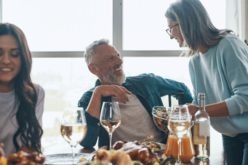 Happy multi-generation family enjoying dinner and smiling while sitting in the modern apartment