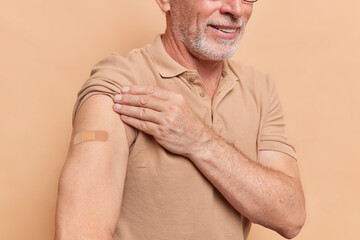 Cropped shot of senior bearded man shows shoulder with adhesive band after vaccination feels good and healthy prevents disease spread. Old people at high risk of getting infected with coronavirus