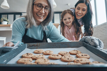 Happy senior woman taking out cookies from the oven and smiling while spending time with family