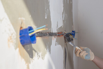 A Caucasian male builder secures an electrical box under an outlet with plaster or alabaster