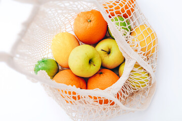 Mesh shopping bag with fresh fruits on light colored background. Zero waste, plastic free concept.