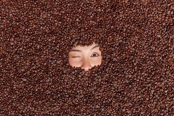 Serious mysterious Asian woman shows only eyebrows and eyes buried in brown roasted seeds being...