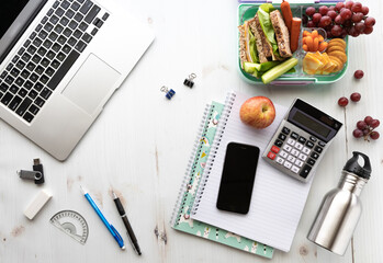 Top down view of a desktop arrangement of a laptop, cell phone and school supplies along with lunch.
