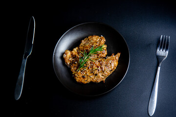Steak on the plate and black background sprinkled with salt and pepper.
