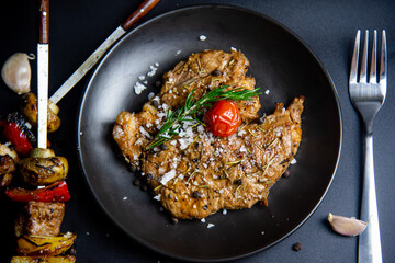 Steak on the plate and black background sprinkled with salt and pepper.
