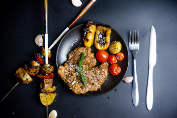 Steak on the plate and black background sprinkled with salt and pepper.
