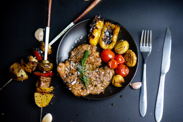 Steak on the plate and black background sprinkled with salt and pepper.
