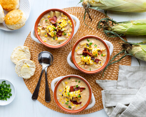 Top down view of chicken and corn chowder in soup crocks topped with grilled corn and bacon, ready for eating.