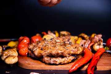 Steak on a wooden cutting board and black background sprinkled with salt and pepper.