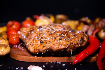 Steak on a wooden cutting board and black background sprinkled with salt and pepper.