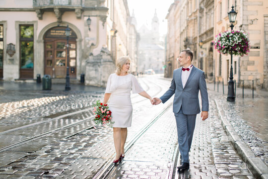 Romantic handsome man and beautiful woman, wearing elegant clothes, enjoying city walk. Portrait of happy middle aged couple in love, holding hands, having a date in ancient city