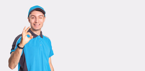 Photo of a smiling delivery man standing in front of camera showing with the gesture everything is fine and winking.