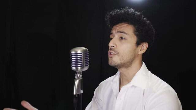 Curly-haired Mexican pop singer singing with a microphone against a black background shot