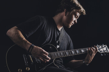 Obraz na płótnie Canvas a guy in a dark T-shirt plays an electric guitar on a dark background