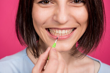 Beautiful happy young woman using interdental brush on the pink background