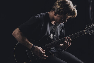 a guy in a dark T-shirt plays an electric guitar on a dark background