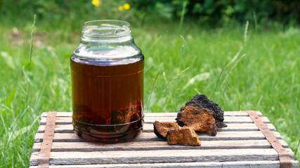 Superfood detox natural chaga mushroom tea in a glass jar with pieces of natural birch mushroom on...