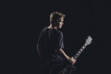 a guy in a dark T-shirt plays an electric guitar on a dark background