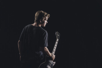 a guy in a dark T-shirt plays an electric guitar on a dark background