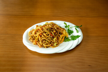 Asian udon noodles with hot sauce, sauteed fruits, vegetables and carrots and chicken meat with parsley on white tray