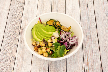 Vegetable salad with coriander, chopped ripe avocado, red onion, roasted cucumbers, whole hazelnuts and lettuce sprouts inside a bowl for home delivery