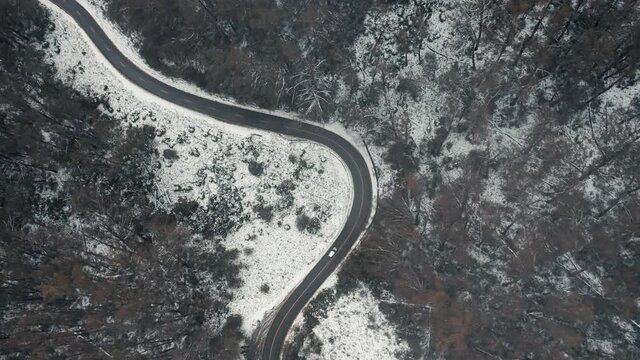 Aerial shot top down cinematic 4k view of white car driving on country road in snow forest at Falls Creek, VIC Australia
