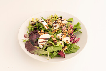 chopped goat cheese salad, assorted lettuce sprouts, peeled and split California walnuts, balsamic vinegar and white plate on a white background