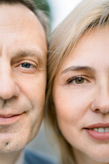 Close up cropped shot of half of faces of handsome middle aged man and stunning attractive blond woman, looking at camera with lovely smiles