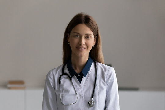 Happy young female doctor, general practitioner, physician, nurse in white coat with stethoscope looking at camera, smiling. Professional portrait of medic worker, medical expert. Head shot