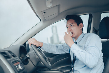 The businessman is eating a sandwich while driving on the road, and he is not without a seat belt.