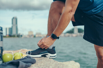 closeup of man tying shoe laces on the stone before running near the beach and city background. Sport and workout concept.