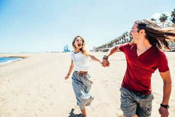 Happy couple enjoying sun holidays running on the beach - Young friends having fun outdoor -...