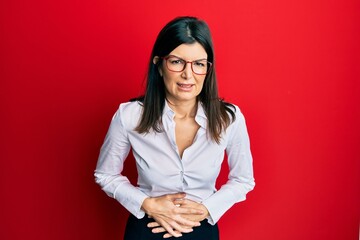 Young hispanic woman wearing business shirt and glasses with hand on stomach because indigestion, painful illness feeling unwell. ache concept.