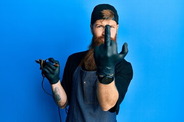 Redhead man with long beard tattoo artist wearing professional uniform and gloves showing middle finger, impolite and rude fuck off expression