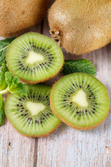 Ripe raw kiwi green whole and slices closeup with mint leaves on aged wooden table.