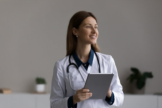 Happy thoughtful female doctor, physician using tablet computer at office, looking away, smiling, thinking. Medic professional using gadget for telemedicine, online consultation. Head shot portrait