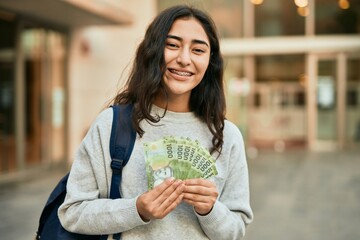 Young middle east student girl smiling happy holding chile pesos banknotes at the city.