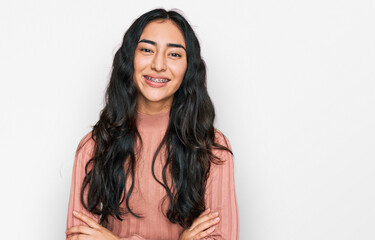 Hispanic teenager girl with dental braces wearing casual clothes happy face smiling with crossed...