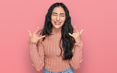 Hispanic teenager girl with dental braces wearing casual clothes shouting with crazy expression...