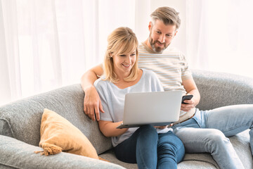 Smiling couple using laptop while sitting on the couch at home