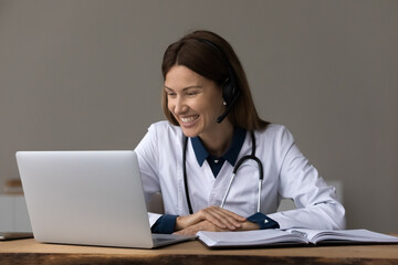 Happy female doctor, physician in headphones giving online consultation, medical help, advice to patient, using laptop for video call, virtual conference. Telemedicine, remote appointment concept - obrazy, fototapety, plakaty