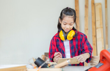 Happy girl standing with noise reduction earmuffs in a carpentry workshop. Children learning in the...