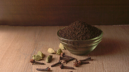 Black Tea Powder or dry dust tea powder, chai patti isolated in wooden bowl with Cardamom, Clove and Ginger.