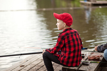 Cute boy in checkered shirt fishing on the lake. Summer outdoor activity concept.